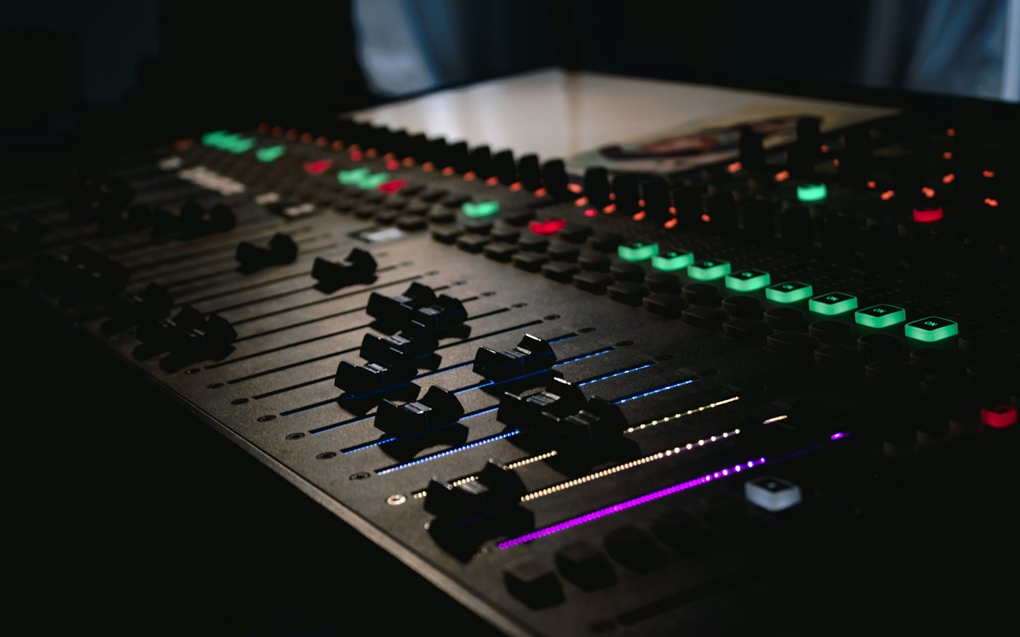 Table de mixage audio avec faders et boutons éclairés.
