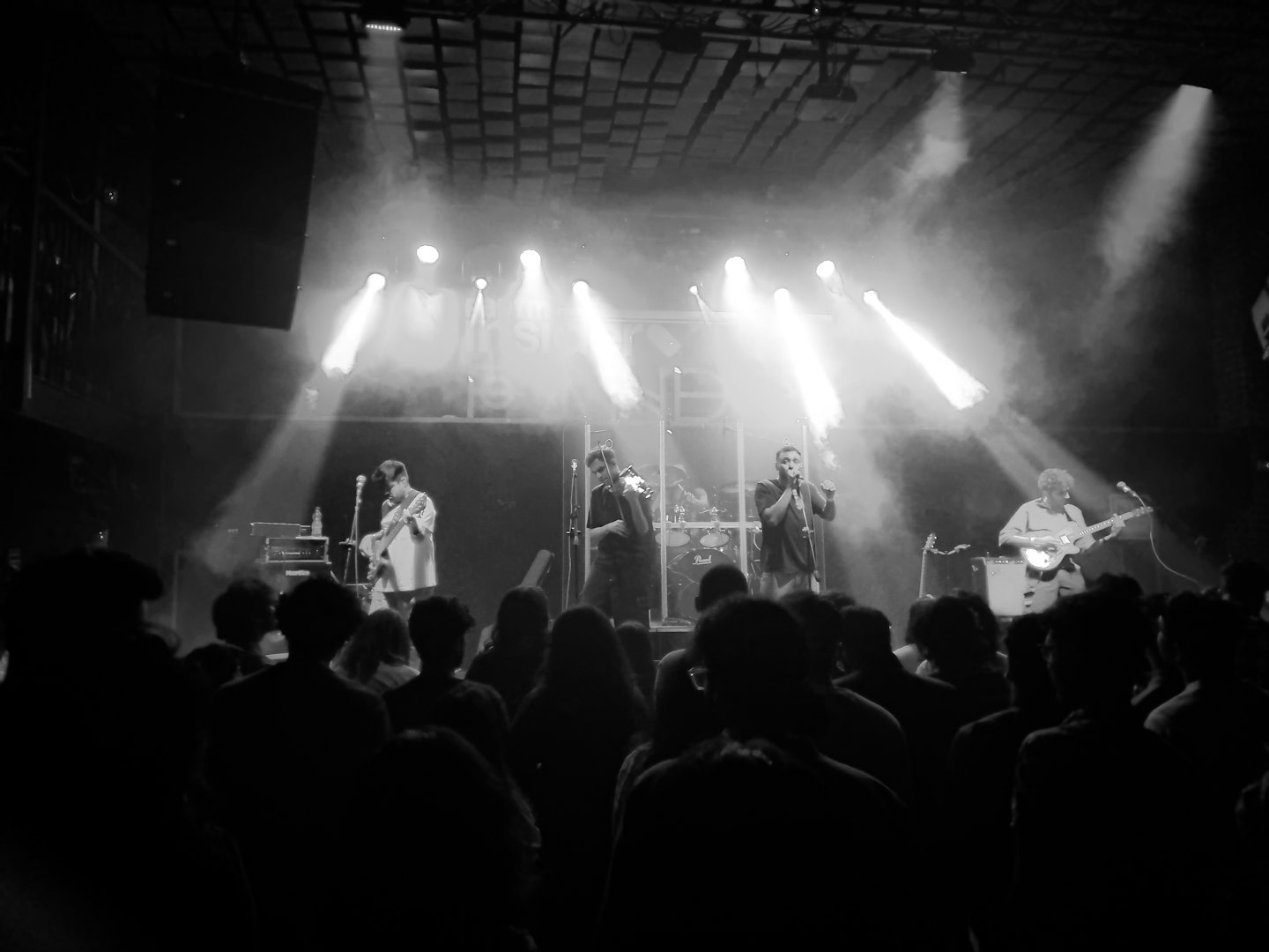 Des musiciens jouent avec énergie sur une scène de concert baignée de lumières vives.