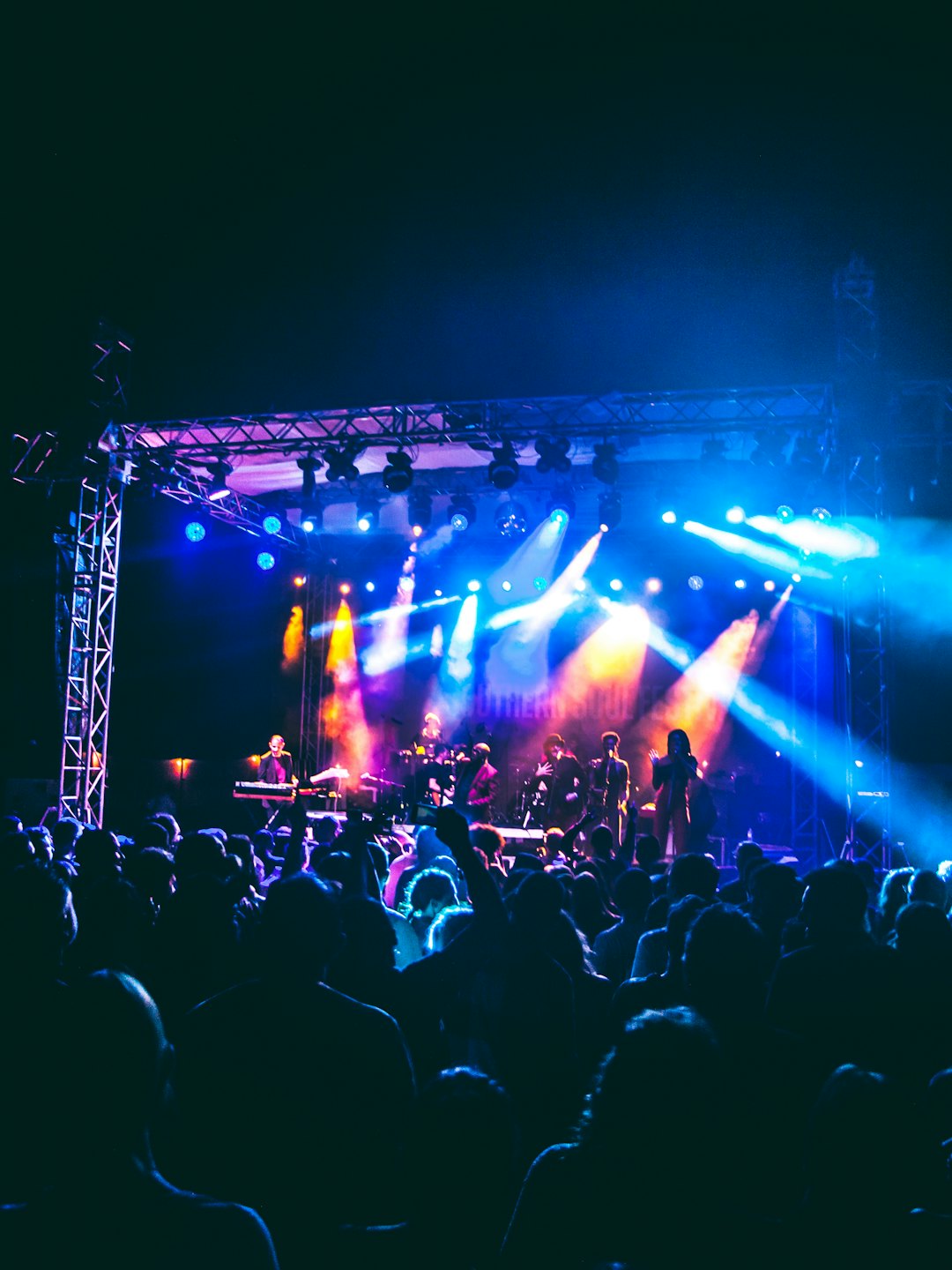 Foule mains levées regardant des musiciens jouer sur scène.